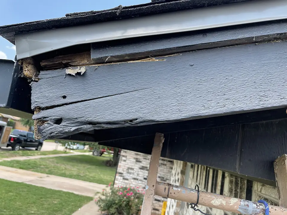 Rotted, broken fascia board along the roof edge of a brick house