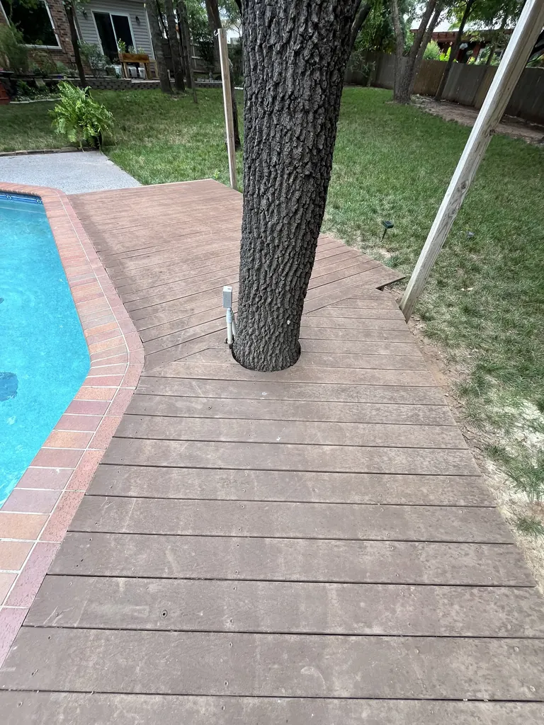 Stained concrete deck with a brick border around a tree beside a pool